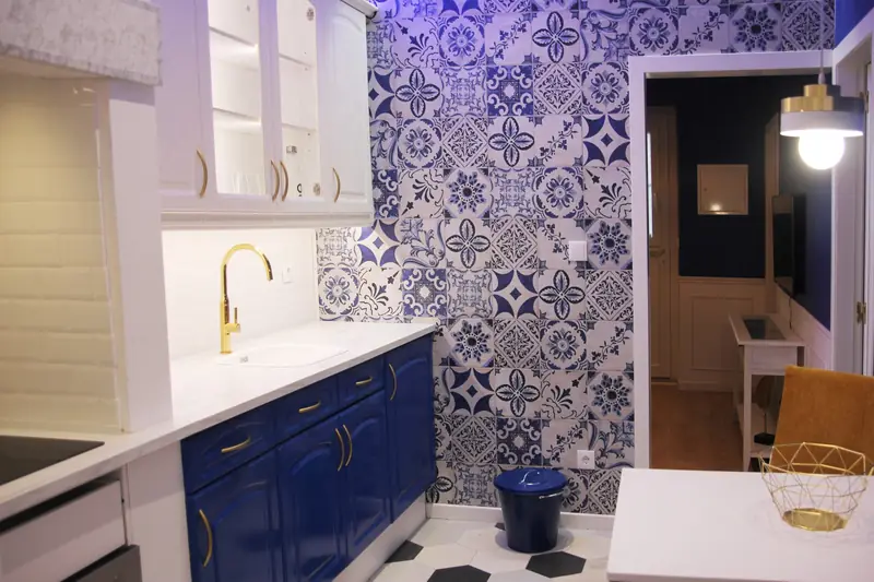Cozinha com armários azuis, puxadores dourados e parede de azulejo português