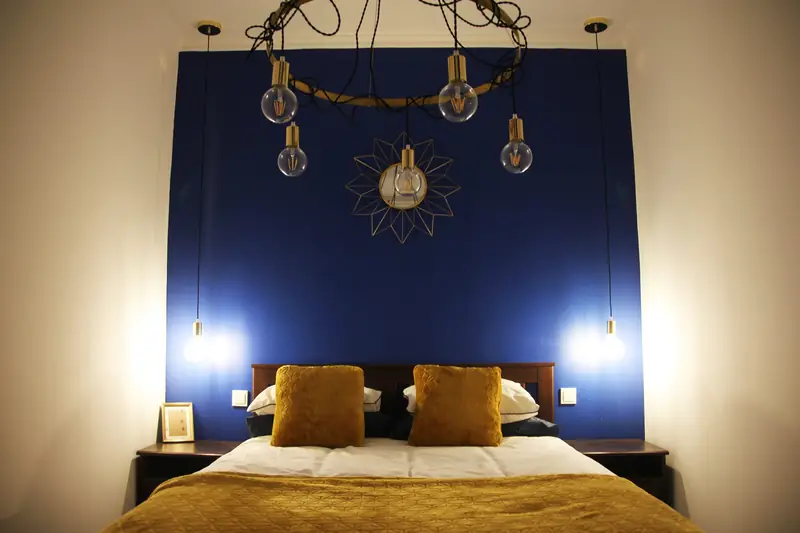 Quarto Celeste à noite: parede azul, lustre de lâmpadas em latão e colcha mostarda