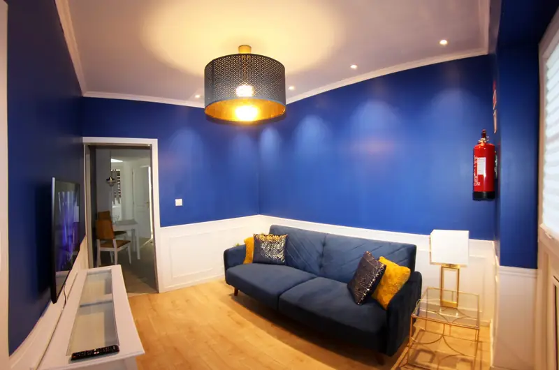 Sala azul com lambril branco, sofá em veludo e candeeiro de teto dourado
