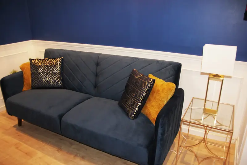 Sofá em veludo azul com almofadas douradas e mesa de apoio em latão